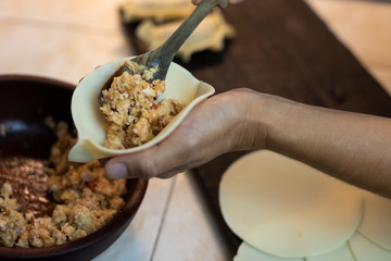 
hands filling pie cover with chicken filling, on table with table and finished pie