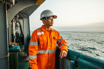Filipino deck Officer on deck of vessel or ship , wearing PPE personal protective equipment - helmet, coverall, lifejacket, goggles. Safety and work at sea. - obrazy, fototapety, plakaty
