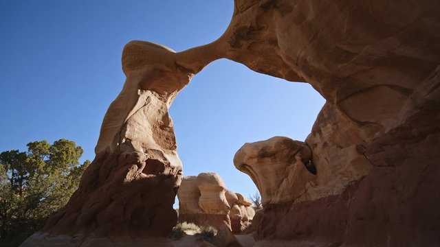 Hiking through and looking up at sandstone Metate Arch in the desert in Grand Staircase Escalante Utah.