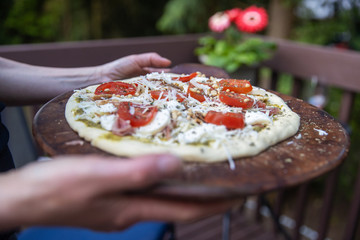 raw pizza with fresh tomato, cheese and pesto outside