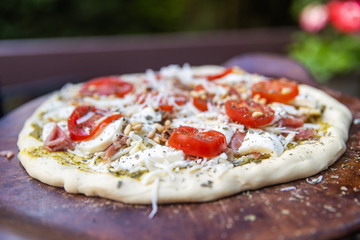 raw pizza with fresh tomato, cheese and pesto outside
