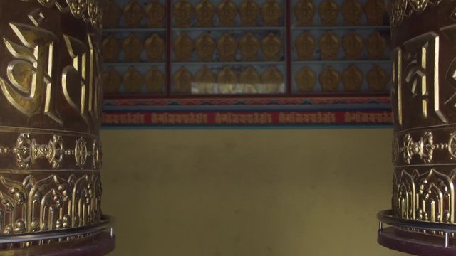 A two golden prayer wheels, with the mantras "om mani padme hum", rotate opposite to each other in tibetan monastery, 