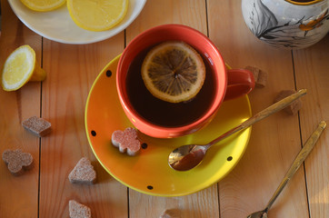 Pleasant and cozy home atmosphere. Tea in a Cup with lemon top view and pieces of brown cane sugar on a wooden table