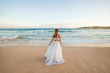Fototapeta na wymiar Bride in a white wedding dress with a veil walking on the sandy caribbean beach at sunny day in Dominican republic 