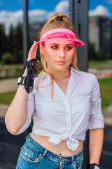 Portrait of an emotional girl in a pink cap visor and protective gloves for rollerblades and...