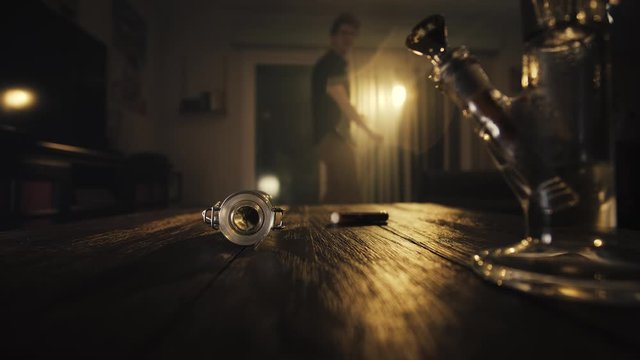 Man pushes table back. On the table, weed and bong slide toward the foreground - weed falls and man goes to pick it up.

Camera Mounted to Table. Fixed Focus. Narrative. 23.976 FPS.