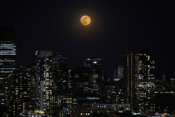 A full moon and night sky over a downtown city skyline.