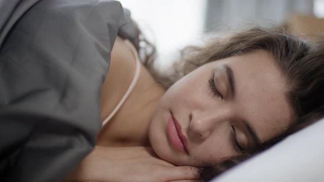 Close up handheld camera shot of pretty young woman with brunette hair sleeping in comfortable bed at home