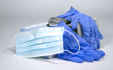 Medical face mask and blue latex gloves for use to protect agains the spread of germs and COVID-19 virus, set against a plain white background.