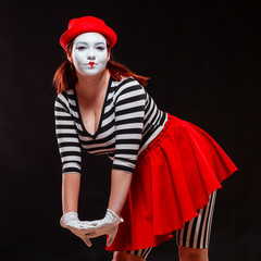 Portrait of female mime artist performing, isolated on black background. Woman in striped clothes...