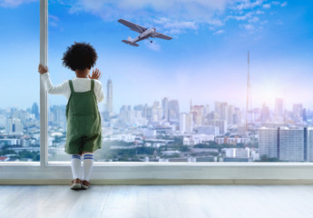 Dark skinned boy looking out of window, airplane flying above city