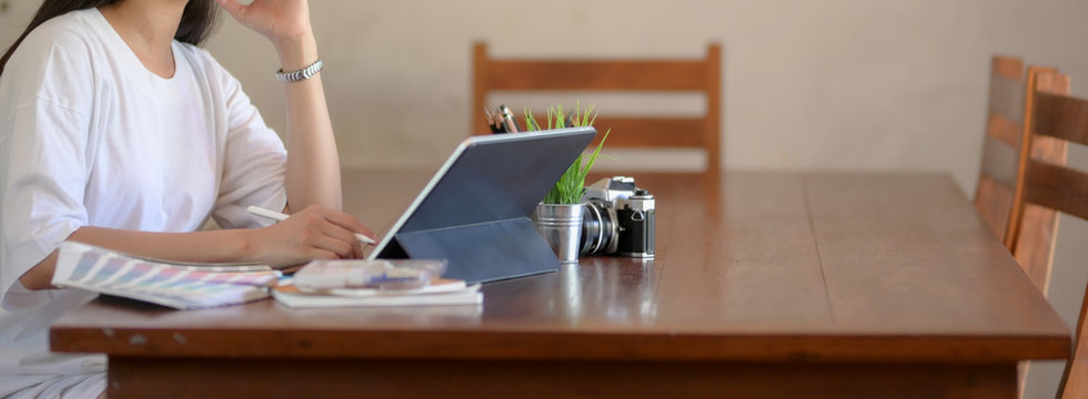 Side View Of Female University Student Doing Her Assignment With Digital Tablet, Camera And Designer Supplies