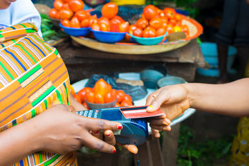black lady shopping in a local market using credit card for payment. Young African trader holding a...