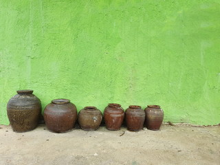 An earthen jar various sizes arranged in rows arranged on a cement floor with a bright green wall...