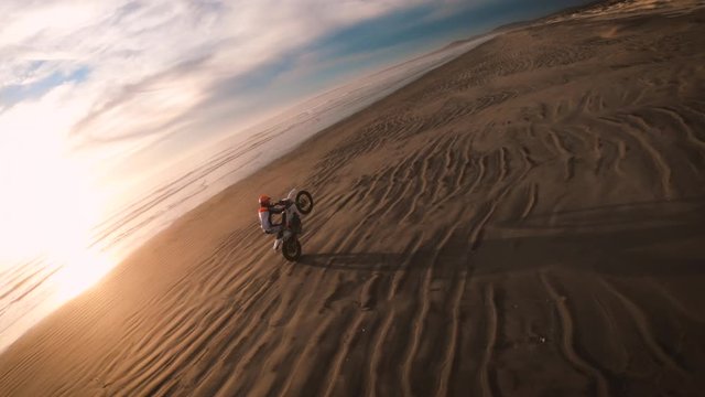 FPV Race Drone Chase of Crazy Motorcycle Stunt Wheelie During Sunset on Beach with Extreme Unique Perspective