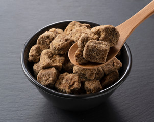 Lift a lump of brown sugar in a black bowl placed on a black background with a spoon