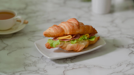 Close up view of a plate of breakfast meal with croissant sandwich ham and cheese