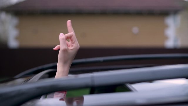 The car hatch opens and a female driver hand with a middle finger sticks out. A woman shows an abusive gesture to another driver. Rudeness on the road.