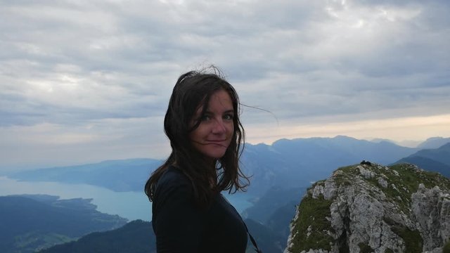 Pretty long hair hiker girl looking at epic view at Schafberg mountain in Salzkammergut Austria. Brunette sexy woman looking at camera and wind blowing. 60fps slowmo footage.