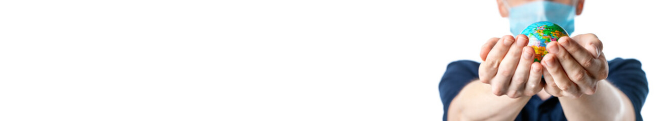 Banner. Close-up of a man's hands holding a small globe, with images Europe, a man in a medical mask out of focus, dressed in a  t-shirt, uniform on a white isolated background, Coronavirus, Covid-19