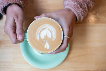 Woman holding Cup of hot art cappuccino coffee on wooden table in cafe shop