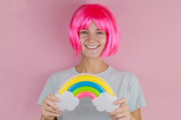 beautiful smiling happy woman with pink hair holding plastic rainbow on a pink background