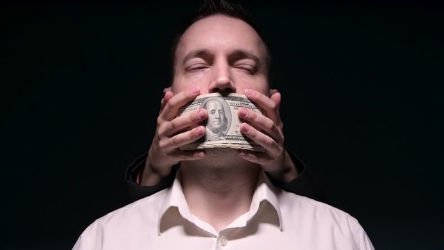 The hands of an unknown woman emerge from the darkness with money and close the eyes of a man in a white shirt. The concept of corruption and bribes in politics and business. Man looks away