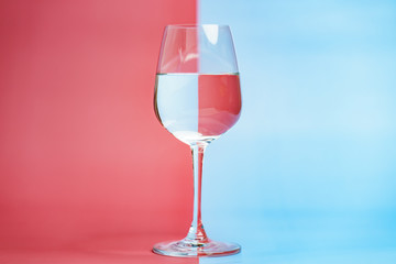 Transparent glass of water, clean drinking water in a clear glass  on two tone (pink and blue) background