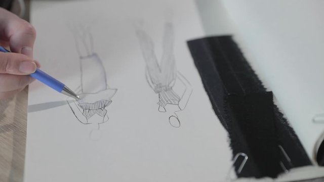 Slow motion video of the girl draws the sketch of future model of clothes in the notebook, tools for sewing, sewing agency, a bunch of flowers, paper craft, top view
