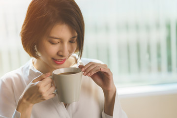 Woman hands holding hot cup of coffee or tea in morning sunlight.