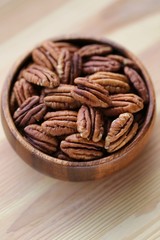 Pecan nuts  in a wooden round cup on a light wooden background.Healthy fats ingredient. Wholesome food and snack.Vegetarian and vegan food.