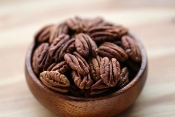 Pecan nuts close-up in a wooden round cup on a wooden background.Healthy fats ingredient. Wholesome food and snack.Vegetarian and vegan food.
