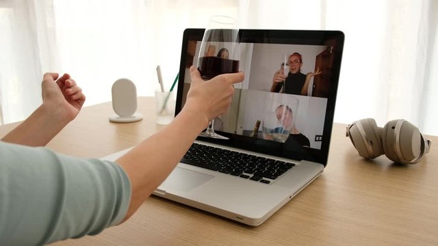 Crop female sitting with glass of wine at table and making video call via laptop with girlfriends while having remote party during coronavirus outbreak