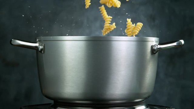 Throwing pasta fusilli into boiled water in pot, shooting with high speed cinematic camera at 1000 fps.
