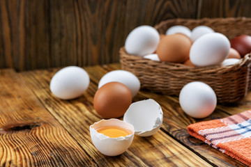 Farm eggs white and brown lie on a wooden table and in a basket, close-up, low light, selective focus, shallow depth of field. Organic food concept