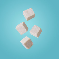 Tofu pieces in motion on blue background . Asian, vegan, protein, healthy food, falling and flying in the air.