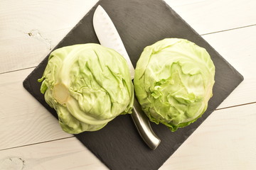 Fresh green cabbage with a metal knife, on a serving plate of slate, on a painted wooden table.