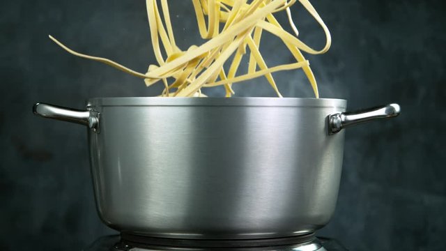 Throwing pasta pappardelle into boiled water in steel pot, shooting with high speed cinematic camera at 1000 fps.