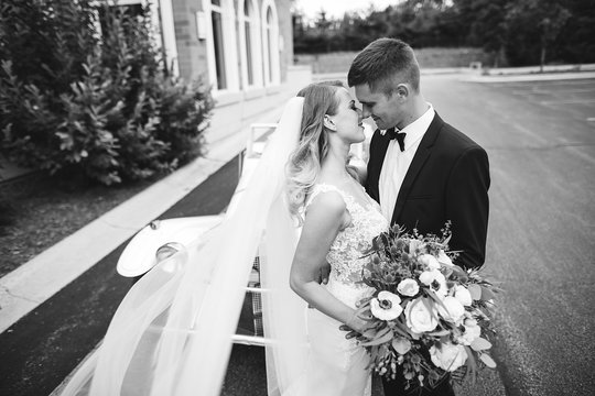 Beautiful Bride In A Long White Dress. Handsome Groom In A Black Suit. Couple Near Old Car