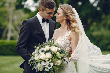 Beautiful bride in a long white dress. Handsome groom in a black suit. Couple in a summer park