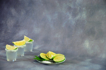 Three glasses of tequila with edges in salt crystals and lime slices on top next to a glass plate...