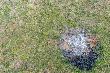 Remains of fire, ashes and cold coals on site of fire on ground covered with green grass. Tourism or picnic in wild. Natural background with copy space and place for text