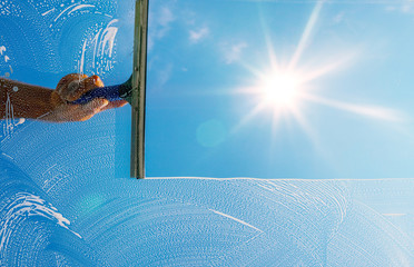 Window cleaner is cleaning window with foam and puller in sunlight