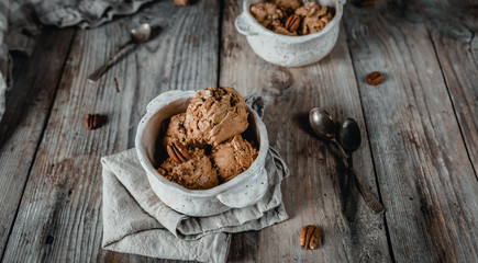 creamy caramel ice cream scoops with pecan nuts in white ceramic bowls on wooden table