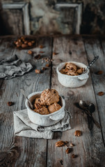creamy caramel ice cream scoops with pecan nuts in white ceramic bowls on wooden table