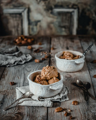 creamy caramel ice cream scoops with pecan nuts in white ceramic bowls on wooden table