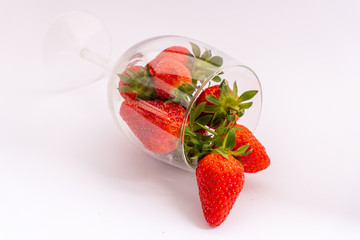 Bunch of juicy strawberries in a lying wine glass on a white background