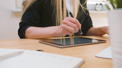 Close-up shot of working on tablet with pen in light office with plants. Business women working on tablet in office.