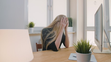 Blond sad female in elegant clothes clutching head after failure or bad news sitting in light...