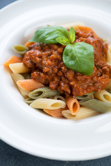 Closeup of italian penne pasta with bolognese sauce and fresh green basil, selective focus, vertical shot
